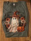  olive green t-shirt featuring a Halloween graphic print of a ghost in a witch hat, a black cat on a pumpkin, and orange flowers.